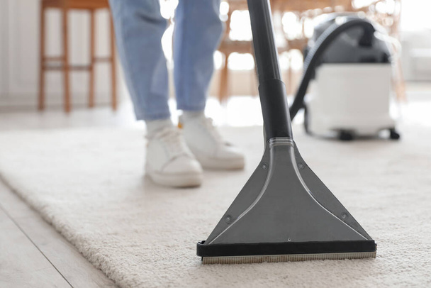 Young woman vacuuming carpet in kitchen - Fotografie, Obrázek
