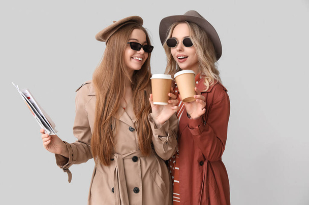 Young sisters with cups of coffee and newspaper on light background - Photo, Image