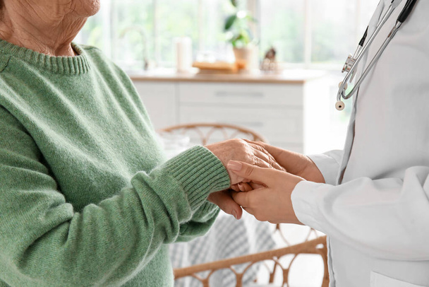 Oudere vrouw met vrouwelijke arts hand in hand thuis, close-up - Foto, afbeelding