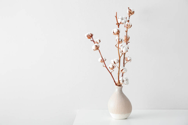 Cotton sprigs in vase on table near white wall - Фото, зображення