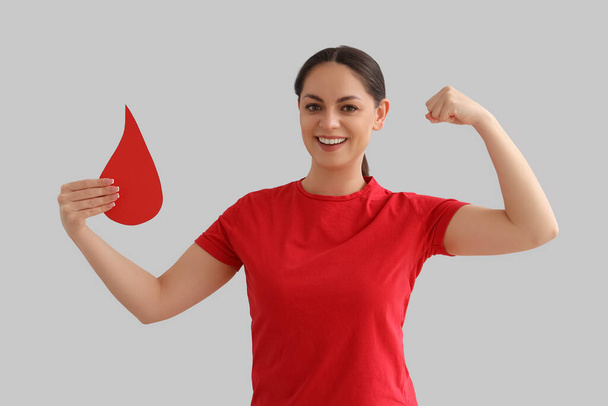 Doador feminino com gota de sangue de papel mostrando músculos em fundo claro - Foto, Imagem