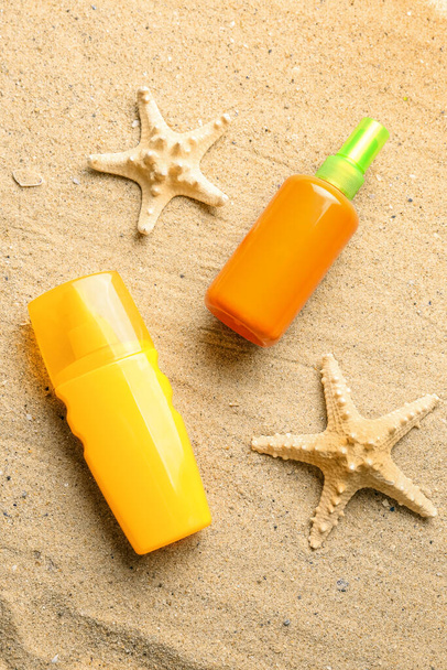 Bottles of sunscreen cream with starfishes on sand - Foto, afbeelding