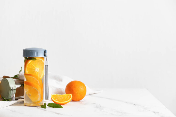 Спортивні пляшки влитої води з апельсиновими скибочками на білому столі
 - Фото, зображення