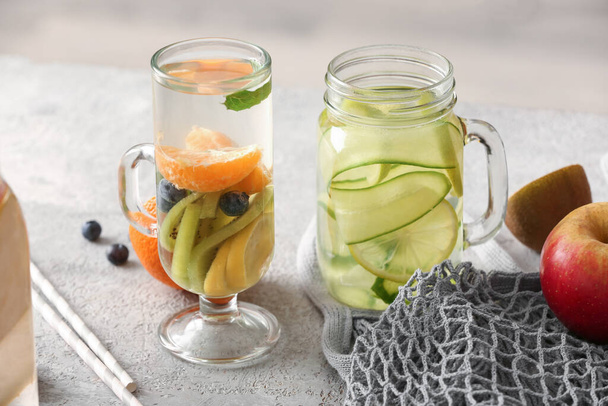 Glass and mason jar of infused water with different sliced fruits on grey table - Foto, immagini