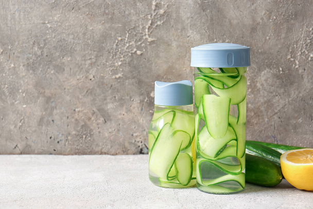 Sports bottles of infused water with cucumber slices on grey table - Photo, image