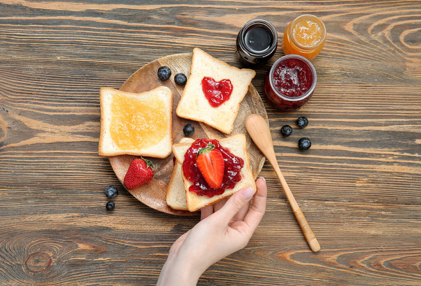 Woman holding delicious toast with strawberry jam and berries on brown wooden background - Foto, imagen