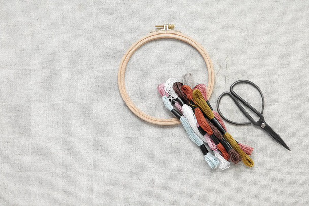 Wooden embroidery hoop with scissors, needles and mouline threads on canvas background - 写真・画像