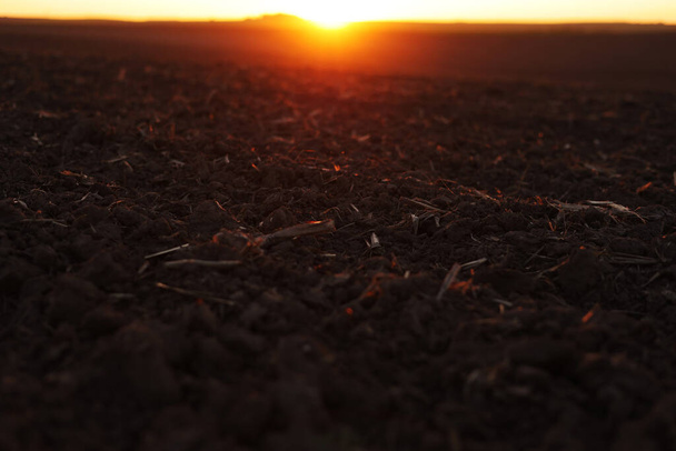 Landwirtschaft und agrarwirtschaftliches Konzept. Schöne ländliche Landschaft Blick auf große gepflügte landwirtschaftliche Feld schwarzer Erde auf orangefarbenen Sonnenuntergang. Vorbereitung landwirtschaftlicher Flächen für die Aussaat von Pflanzen und das Pflanzen von Gemüse - Foto, Bild