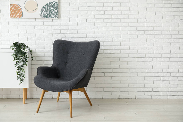 Dark grey armchair with dresser, painting and houseplant near white brick wall - Photo, Image