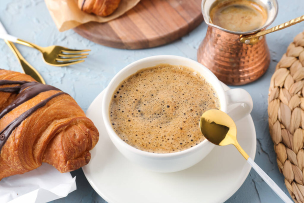 Cup of delicious espresso with jezve and croissant on blue background - Photo, Image