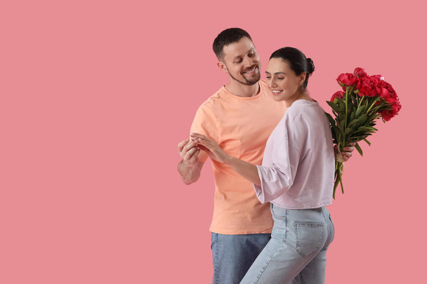 Young man putting engagement ring onto his girlfriend's finger on pink background - Photo, Image