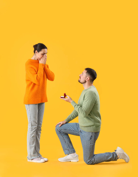 Young man proposing to his girlfriend on yellow background - Foto, afbeelding