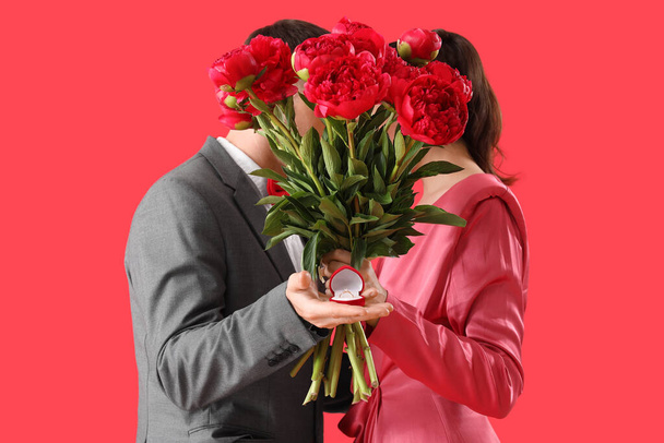 Young couple with engagement ring and flowers on red background - Photo, Image