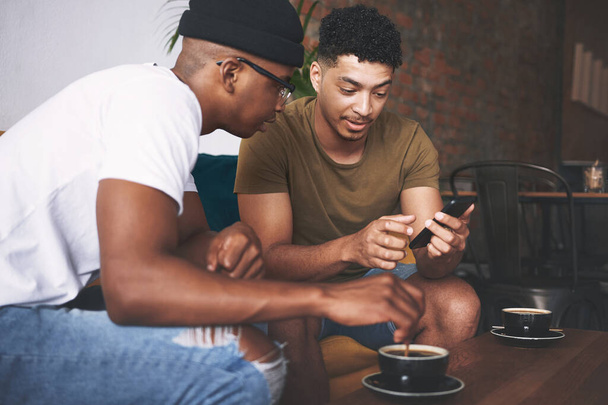 This is that dating app I was telling you about. men discussing something on a cellphone while sitting together in a coffee shop - Fotoğraf, Görsel
