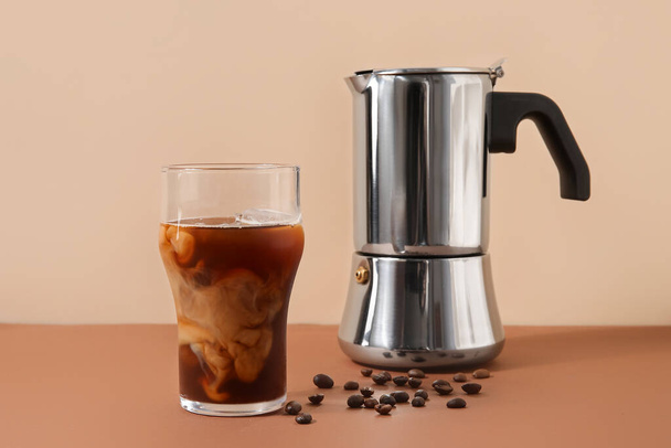 Glass of ice coffee with beans and geyser coffee maker on table near beige wall - Фото, изображение