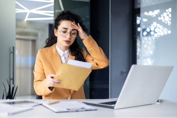 Dissatisfied and upset businesswoman received letter in envelope, depressed latin american businesswoman reading notification message, at work inside office with laptop. - Photo, Image