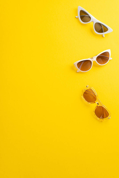 Delicie-se com a temporada de verão com esta atraente vista vertical superior flat lay. Diferentes tipos de óculos de sol em um fundo amarelo brilhante, com um espaço vazio para o seu texto ou anúncio - Foto, Imagem