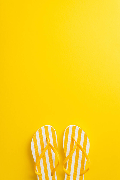 Delight in the beauty of summer with this eye-catching top vertical view flat lay. Discover a pair of flip-flop shoes on a bright yellow background, with a blank space for your text or advertisement - Foto, Imagen