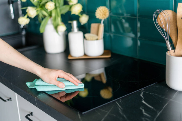 cropped shot of female hand with microfiber rag cleaning glass ceramic electrical hob on marble countertop in stylish kitchen, housework concept - Photo, image