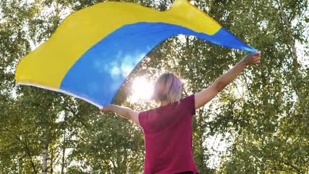 Nainen hurraa Ukrainan lippu selässään. Iloinen nainen, jolla on lippu käsissään. Ukrainan voitto heiluttaen lippu - Materiaali, video