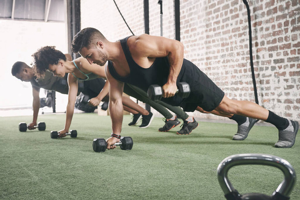 Fortalece tu agarre. un grupo de fitness que usa pesas mientras hace flexiones en el gimnasio - Foto, Imagen