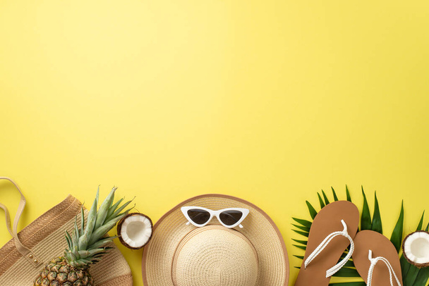 Exploring summer destinations. Top view shot of coastline essentials, glasses, sunhat, beach bag, flip-flops, exotic fruits, palm leaves on yellow backdrop. Ideal for travel campaign or text placement - Photo, Image