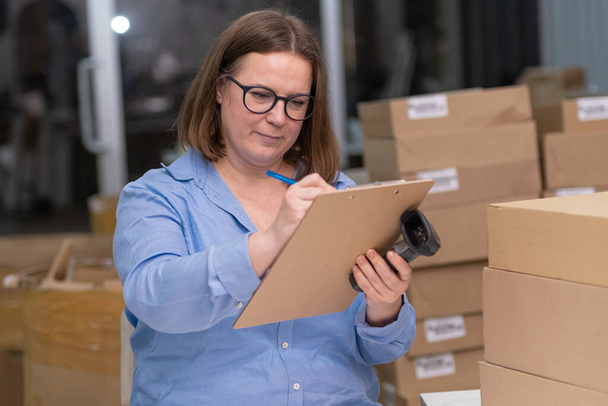 vrouwelijke kleine ondernemer van een online winkel, controleren en bijhouden van bestellingen, terwijl ook het beheer van product zendingen en verpakkingen. - Foto, afbeelding