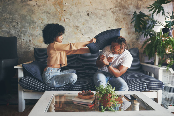 Deja de tomarme el pelo. una pareja joven teniendo una pelea de almohadas mientras se relajan juntos en un sofá en casa - Foto, imagen