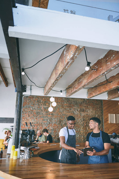 Растущая прибыль за счет командной работы и страсти к кофе. двое молодых людей, работающих в кафе с цифровой планшеткой - Фото, изображение