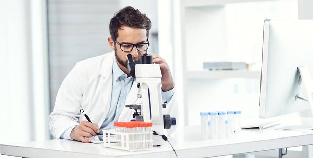 Deneği gözlemliyorum. Odaklanmış genç bir bilim adamı mikroskop altında ve laboratuarda otururken notlar alıyor. - Fotoğraf, Görsel