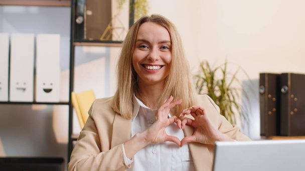 I love you. Young business woman makes symbol of love, showing heart sign to camera, express romantic feelings, express sincere positive feelings at home office workplace. Charity, gratitude, donation - Foto, afbeelding
