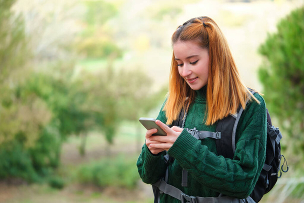 Szczęśliwy ruda młoda kobieta turysta konsultingu smartfon podczas trekking. Koncepcja turystyki pieszej. - Zdjęcie, obraz