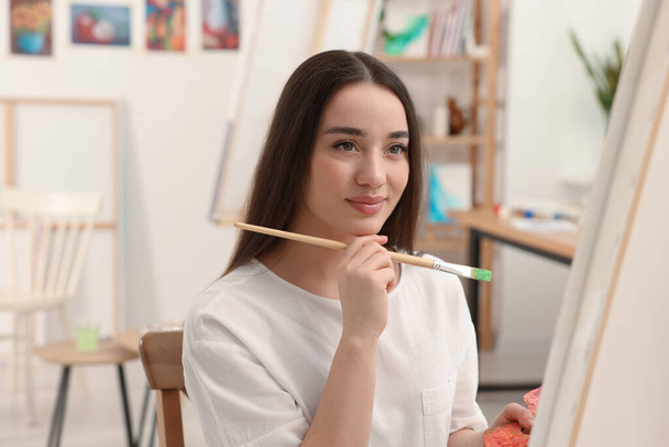 Beautiful young woman painting with brush in studio. Creative hobby - 写真・画像