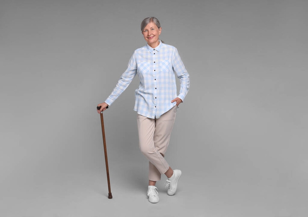 Senior woman with walking cane on gray background - Foto, Imagem