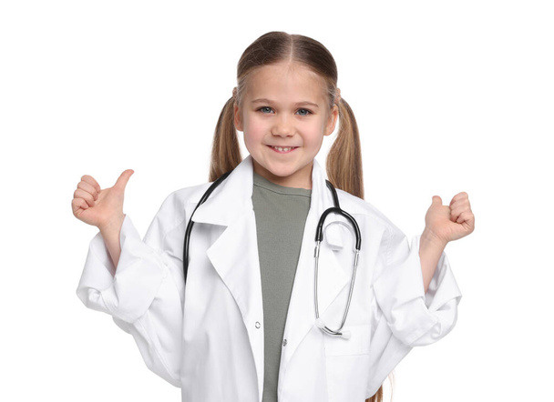 Little girl in medical uniform with stethoscope showing thumbs up on white background - Fotoğraf, Görsel