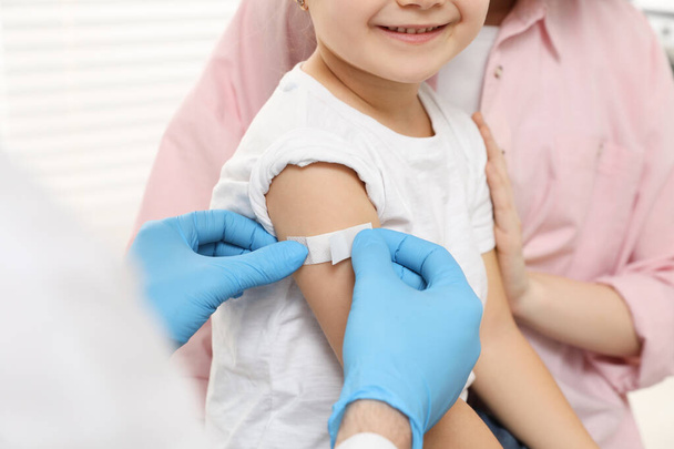 Children's hepatitis vaccination. Mother with her daughter in clinic. Doctor sticking medical plaster on little girl's arm, closeup - Valokuva, kuva