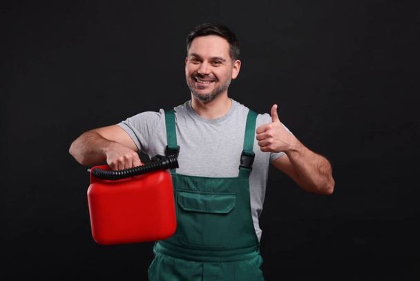 Man holding red canister and showing thumbs up on black background - Foto, imagen