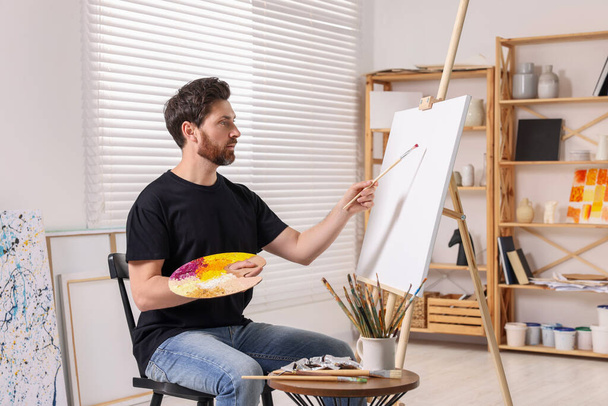 Man painting in studio. Using easel to hold canvas - Fotoğraf, Görsel