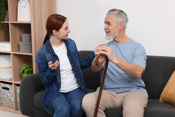 Caregiver and senior man with walking cane on sofa at home - Photo, image