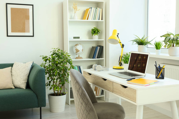 Cozy workspace with modern laptop on white wooden desk and comfortable chair at home - Foto, Imagen