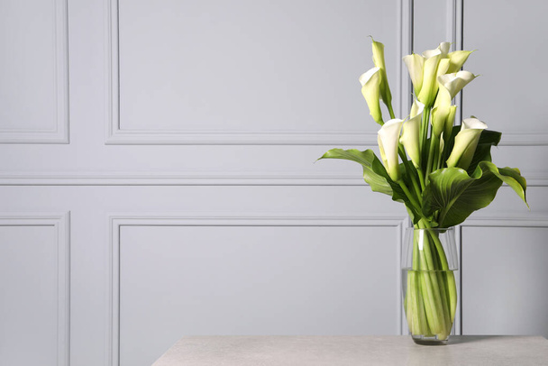 Beautiful calla lily flowers in vase on table, space for text - Fotó, kép