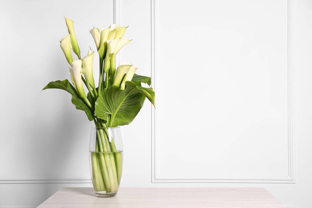 Beautiful calla lily flowers in vase on table, space for text - Photo, Image