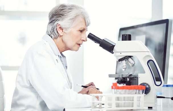 Tengo que concentrarme cada vez que hago esto. una científica anciana enfocada mirando a través de un microscopio mientras está sentada en un laboratorio - Foto, imagen