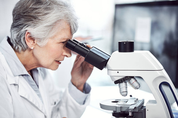Faire des percées médicales. une scientifique âgée concentrée regardant à travers un microscope alors qu'elle était assise dans un laboratoire - Photo, image