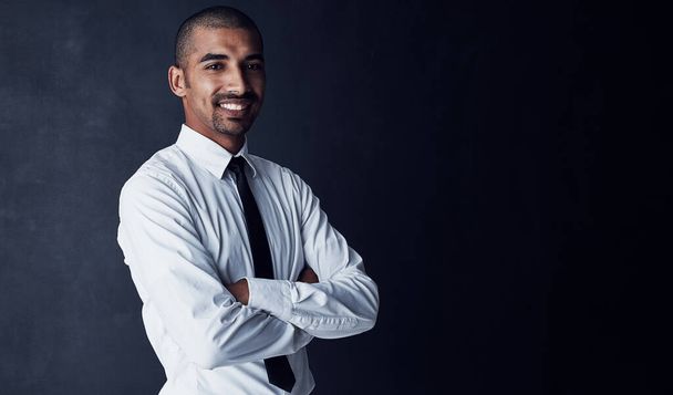 Confidence sets the stage for success. Studio portrait of a confident young businessman against a dark background - Photo, image