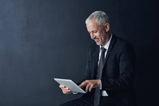 Staying efficient, staying informed. Studio shot of a mature businessman using a digital tablet against a dark background - Фото, зображення
