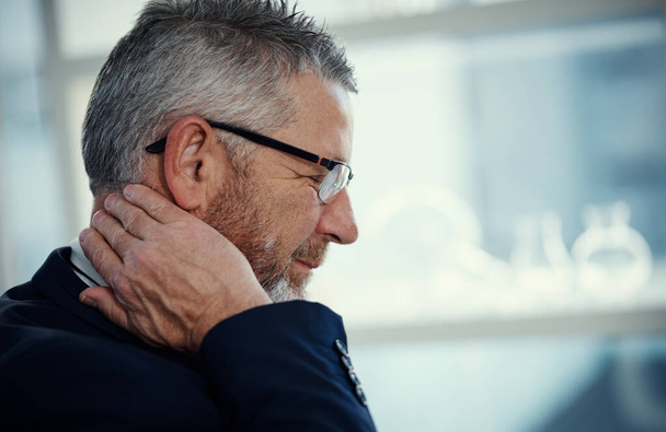 His neck is baring the brunt of stressful business. a mature businessman experiencing neck ache at work in a modern office - 写真・画像