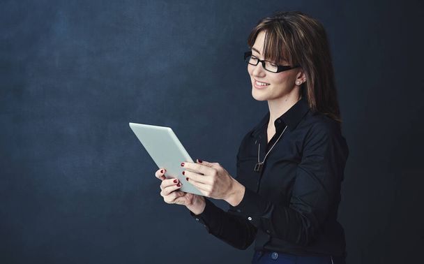Organising her plans for success the smart way. Studio portrait of a corporate businesswoman using a digital tablet against a dark background - Fotó, kép