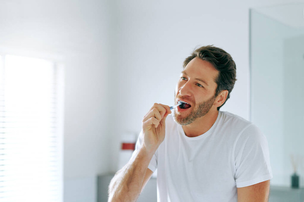 Starám se o zuby, abych si je mohl nechat déle. pohledný muž středního věku si doma čistí zuby v koupelně - Fotografie, Obrázek
