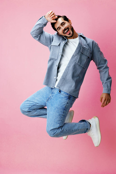Uomo di moda con la barba che salta su sfondo rosa in t-shirt e jeans bianchi, sorriso ed emozione gioiosa sul viso, full-length, spazio copia. Foto di alta qualità - Foto, immagini